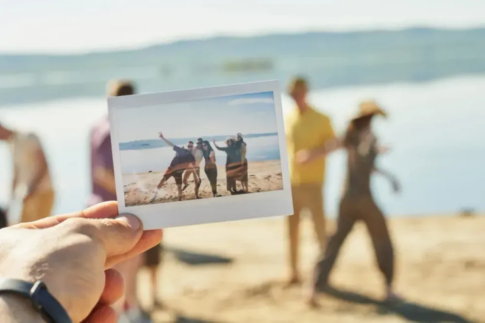 Person holding a polaroid photo of friends posing in a group up to the camera while the friends in the photo disperse in the background